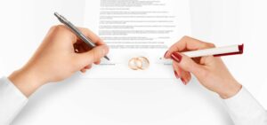 Man and woman sign prenuptial agreement near gold rings. Legal prenup document contract signing by newlywed couple. Marry partners signature on prenupt statement. Wedding ceremony conflict text.