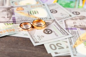 Two gold wedding rings placed on top of scattered US dollar bills, symbolizing the financial aspects of divorce and alimony.
