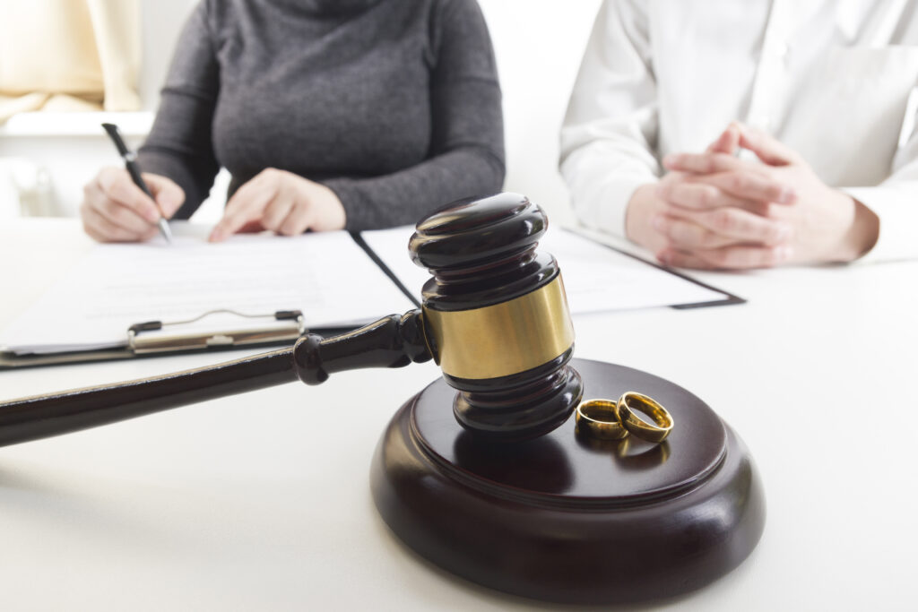 Judge’s gavel with wedding rings in front, as a couple signs divorce documents during legal proceedings